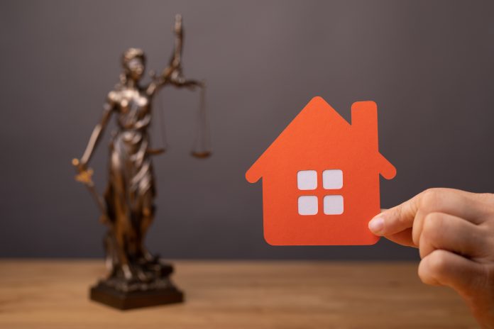 Selective focus of a person's hand holding a red estate sign and the statue of law on the background