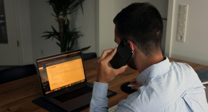 man using mobile phone in front of laptop